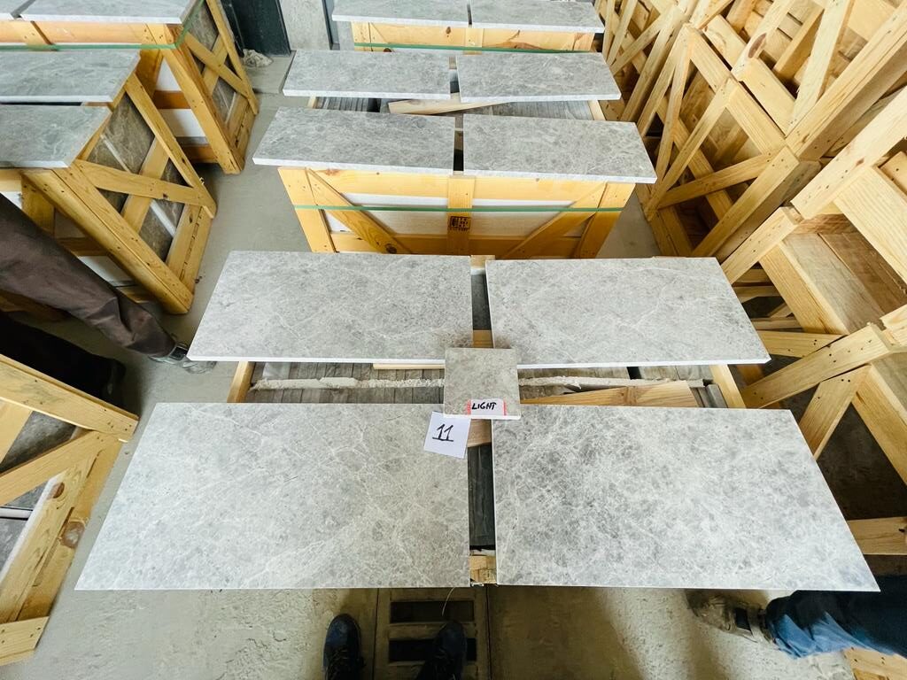 Grey marble tile pieces from a crate laid out on a factory floor for a selection check, with a numbered label and a sample piece