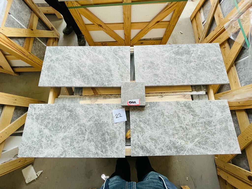 Grey marble tile pieces laid out on a crate for a selection check, with a numbered label and a sample piece