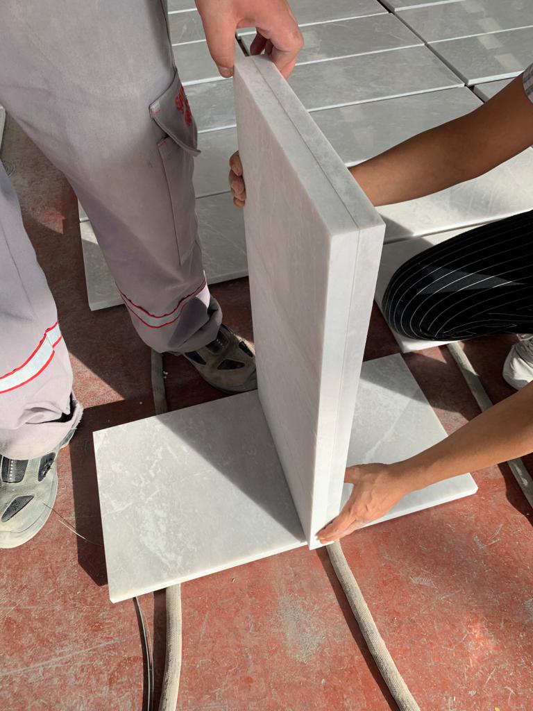 Two inspectors checking a marble tile held upright against a flat tile to test squareness